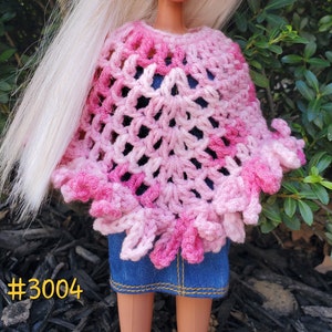 Puede incluir: Un poncho de crochet rosa y blanco con un borde festoneado. El poncho está hecho con un delicado patrón de punto abierto.