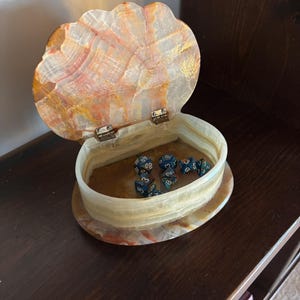 May include: A white and brown, shell-shaped, onyx box with a hinged lid. The box is open and contains several blue and silver dice.
