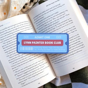 Puede incluir: Un marcapáginas azul y rojo con forma de boleto para el Club de Lectura Lynn Painter, con los títulos "Better Than The Movies", "Mr. Wrong Number" y "Fake Skating", descansa sobre un libro abierto.