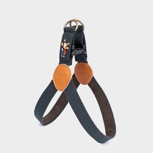 May include: A navy blue dog harness with brown leather accents and a pixelated design. The harness features a metal ring, a black plastic buckle, and the brand name "HOWLPOT" on a leather patch.