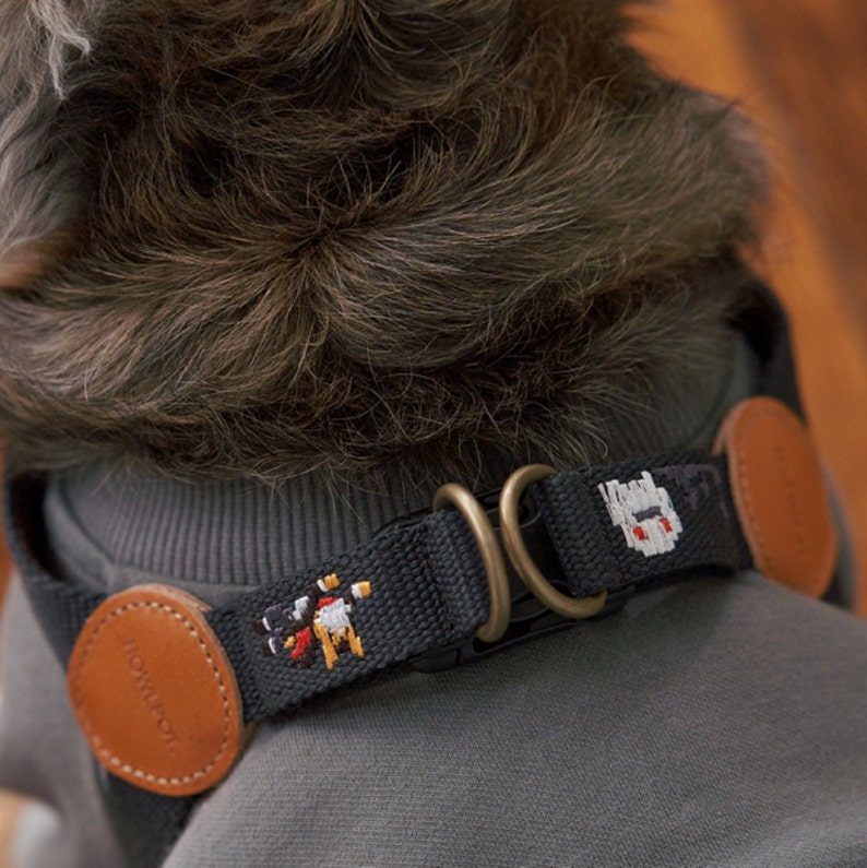 May include: Black dog collar with embroidered pixelated designs. The collar features brown leather accents and brass-colored metal hardware. The collar has a pixelated design of a knight and a monster. The brand name "HOWL BOT" is visible on the leather accent.