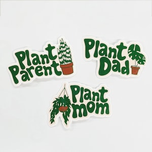 Puede incluir: Tres pegatinas con texto verde sobre fondo crema. Las pegatinas dicen "Plant Parent", "Plant Dad" y "Plant Mom". Cada pegatina tiene una ilustración de planta diferente: un cactus, una monstera y una planta colgante.
