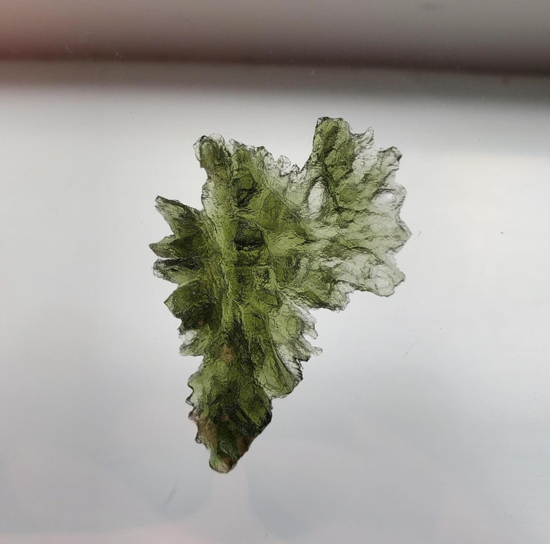 May include: A green, translucent, crystalline rock with a unique, jagged, and irregular shape.