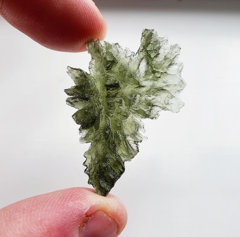 May include: A green, translucent, crystalline rock with a unique, irregular shape. The rock has a rough, textured surface and appears to be a natural formation.
