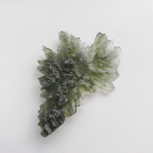 May include: A green, translucent, crystalline formation with a jagged, irregular shape. The crystal has a rough, textured surface and appears to be made of multiple smaller crystals fused together.
