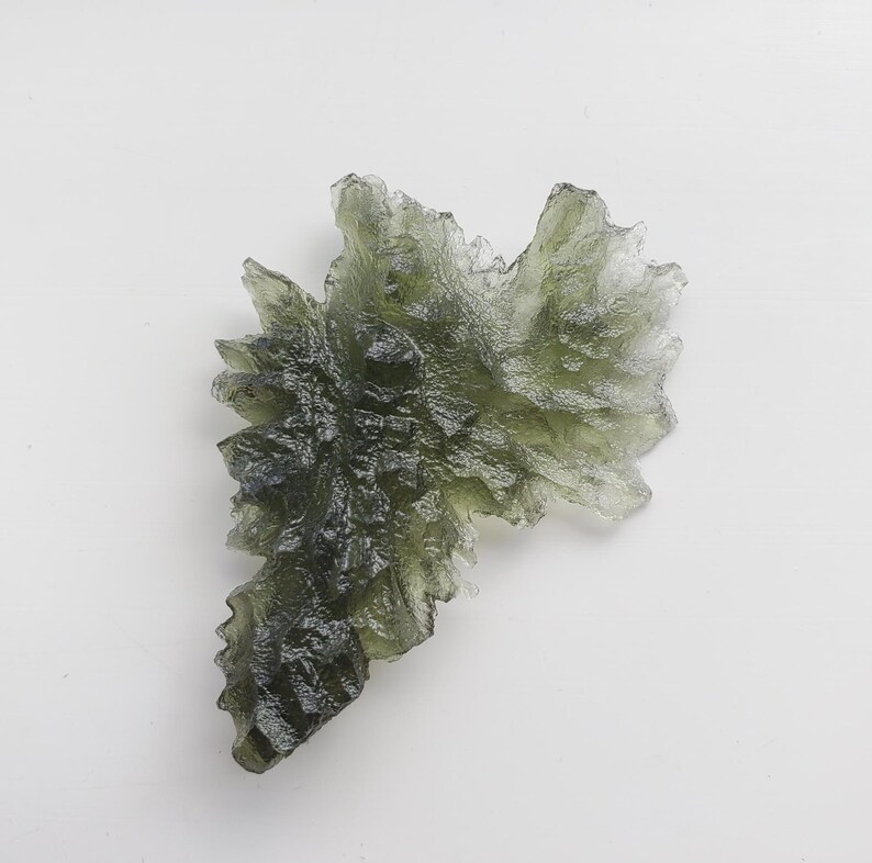 May include: A green, translucent, crystalline formation with a jagged, irregular shape. The crystal has a rough, textured surface and appears to be made of multiple smaller crystals fused together.