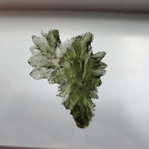 May include: A large, green, crystalline formation with a rough, textured surface. The crystal is shaped like a leaf or a fern.