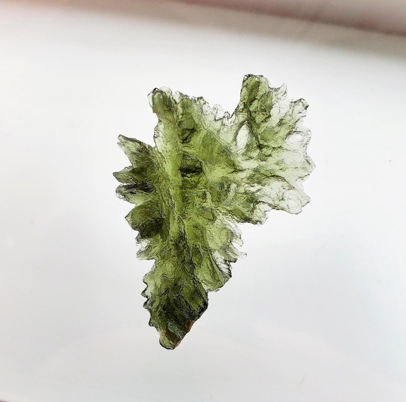 May include: A green, translucent, and irregularly shaped crystal with a rough, jagged texture. The crystal is a natural formation and has a unique, organic shape.