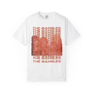 May include: White t-shirt featuring the band name "The Bangles" in orange text. The design includes a graphic of the band members in orange, with the band's name repeated vertically.