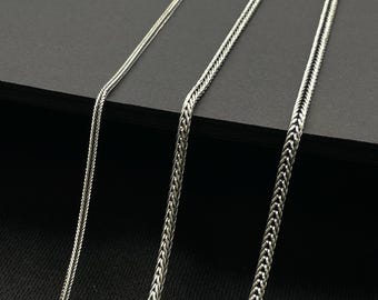 May include: Three silver chains of varying widths and lengths, displayed against a black background. The chains are made of a fine, delicate metal and have a smooth, polished finish.