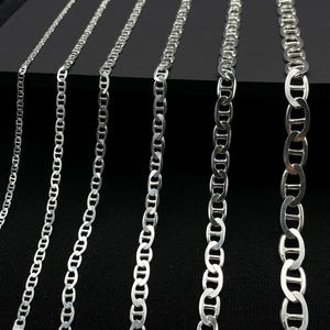 May include: Six silver mariner chain necklaces of varying widths, laid out on a black surface.