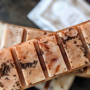 May include: A close-up of a wax melt bar with a brown and white marbled design and brown flecks. The bar is divided into six sections.