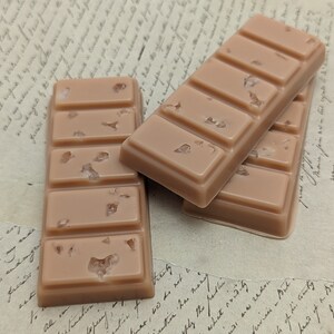 May include: Three rectangular bars of brown wax with a light brown color and flecks of white throughout. The bars are stacked on top of each other.