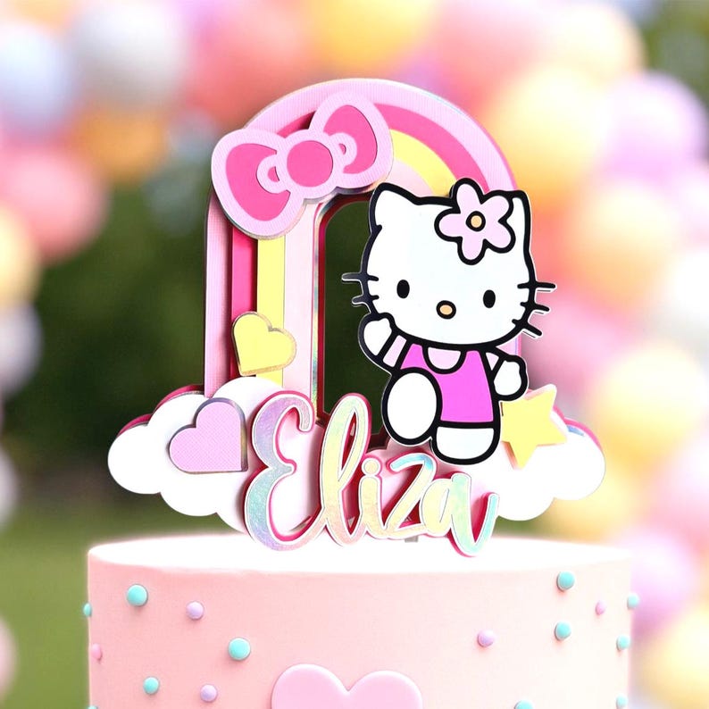 Może przedstawiać: R&oacute;żowo-ż&oacute;łty topper na tort w kształcie tęczy z postacią Hello Kitty, r&oacute;żową kokardką i imieniem "Eliza" w mieniących się literach.