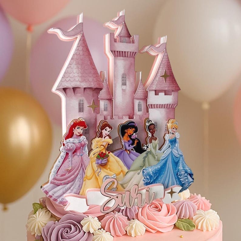 May include: A pink castle cake topper with five Disney princesses, including Ariel, Belle, Jasmine, Tiana, and Cinderella. The topper is decorated with gold stars and the name "Suri" is written on a banner.