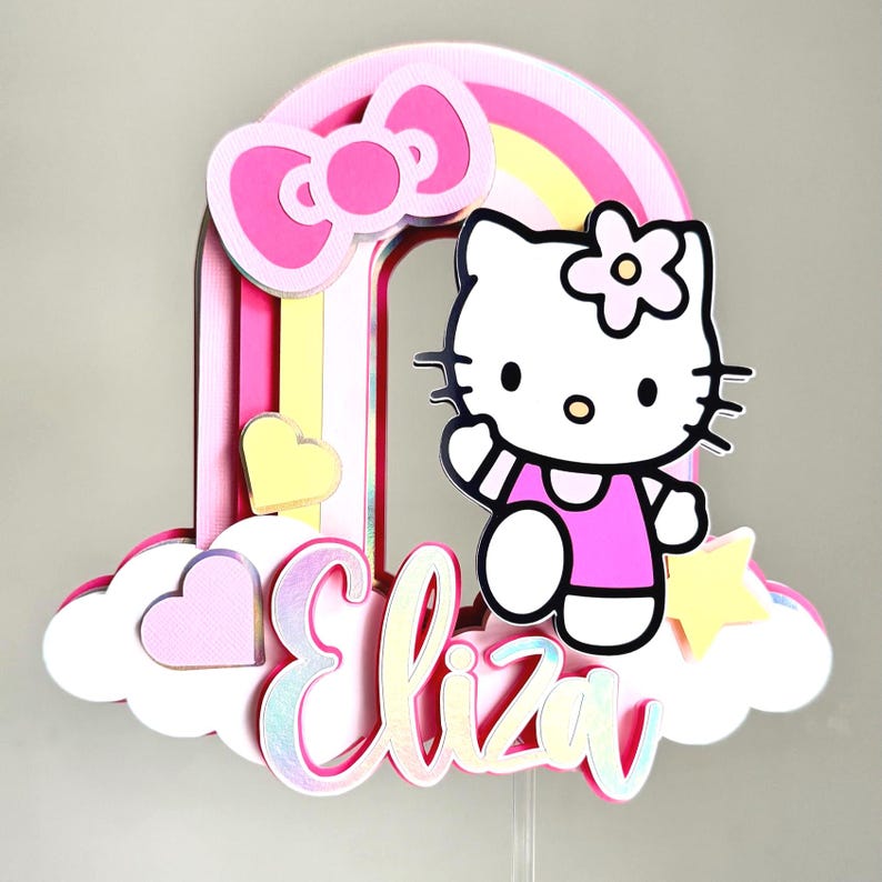 Może przedstawiać: Topper na tort w kształcie tęczy w kolorze r&oacute;żowym i ż&oacute;łtym z postacią Hello Kitty, r&oacute;żową kokardką i imieniem "Eliza" w r&oacute;żowych literach z brokatem.