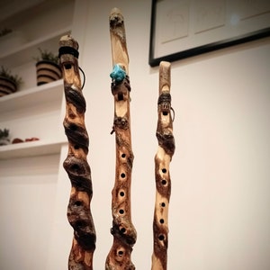 May include: Three wooden flutes with decorative details, including a turquoise stone on the top of the middle flute. The flutes are standing upright on a wooden base.