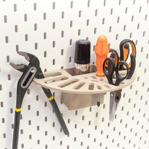 Può includere: Un organizer beige per pannello forato con vari strumenti. Include pinze nere e gialle, forbici nere, uno strumento arancione, una bomboletta spray nera e una penna d'argento. L'organizer è montato su un pannello forato bianco.