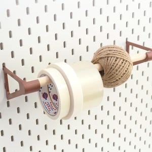 Peut inclure: Un organisateur d'artisanat monté sur un panneau perforé blanc. Il contient des rouleaux de ruban adhésif, une pelote de ficelle et une cheville en bois. L'organisateur a des supports en métal marron.