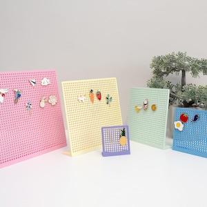 May include: A selection of colourful pin display boards in pink, yellow, green, and blue. Each board is perforated and holds decorative pins, including a rabbit, carrot, and fried egg. A small bonsai tree is in the background.
