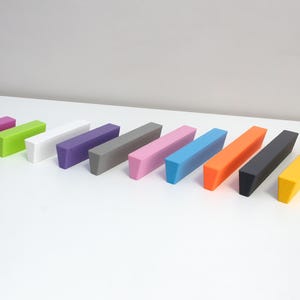 May include: Ten rectangular blocks in a row, in shades of pink, green, white, purple, grey, and blue. The blocks are on a white surface, with a light grey background. Each block is a different colour.