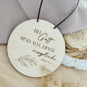Könnte beinhalten: Runder Holzschild mit dem deutschen Text "Bei Gott sind alle Dinge möglich" und dem Bibelvers Markus 10,27. Das Schild hat eine dunkelbraune Lederschlaufe und eine botanische Illustration. Der Hintergrund umfasst ein graues Tuch und eine Holzoberfläche.