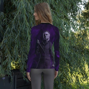 May include: A purple long-sleeve shirt with a graphic print of a masked figure holding a knife. The figure is in a dark, shadowy setting.