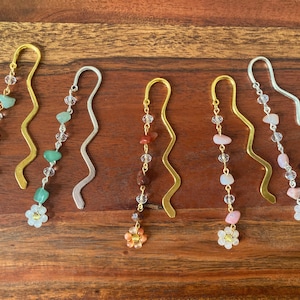 May include: Six gold and silver bookmark pendants with a flower charm at the bottom and a chain of clear beads and coloured stones. The stones are green, red, pink, and brown.