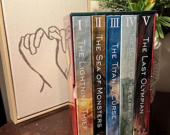 May include: A boxed set of five books from the Percy Jackson series, including "The Lightning Thief" and "The Last Olympian." The spines are in various colours, with the author's name at the bottom. A canvas art piece with a hand gesture is to the left.