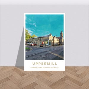 Puede incluir: Una impresión enmarcada que muestra una calle con un edificio de piedra y un cielo azul turquesa. La impresión incluye el texto "UPPERMILL" y "Saddleworth Museum & Gallery". La imagen está sobre un suelo de madera.
