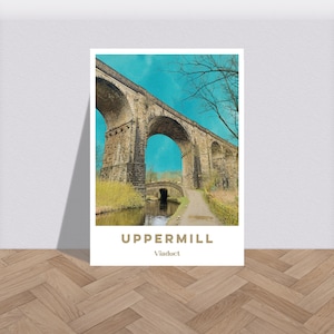 Puede incluir: Un viaducto de piedra con un cielo azul y árboles verdes en el fondo. El viaducto está sobre un canal con un camino que conduce a él. El texto "UPPERMILL Viaduct" está en la parte inferior de la imagen.