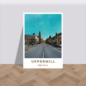 Puede incluir: Un póster de estilo vintage con una foto de una calle en Uppermill, Inglaterra. La calle está bordeada de edificios de ladrillo y se puede ver un campanario de iglesia en la distancia. El texto "Uppermill" y "High Street" está impreso debajo de la foto.