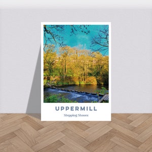 Puede incluir: Una fotografía panorámica de un río con piedras para cruzar en un entorno boscoso. Los árboles son una mezcla de hojas verdes y amarillas, y el cielo es azul. El texto "Uppermill Stepping Stones" está en la parte inferior de la imagen.