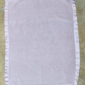 May include: A soft, lavender baby blanket with a satin trim. The blanket has a textured, quilted pattern.