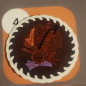 May include: A circular, brown and orange sticker with a white, saw-tooth border. The sticker features a steampunk-style design with gears and mechanical elements. A white circle with the number "4" is in the upper left corner.