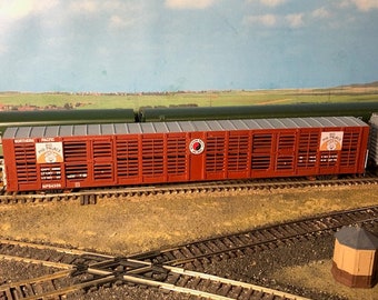 Op de afbeelding: Een rode en bruine veewagen met een grijs dak. De wagen is gelabeld met "Northern Pacific" en "Pig Palace".