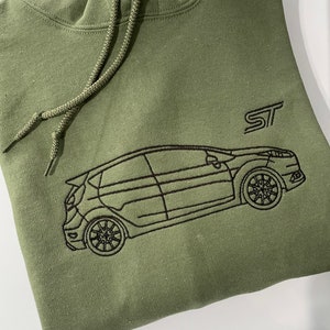 Puede incluir: Sudadera con capucha verde oliva con cordón. La parte delantera presenta un contorno bordado en negro de un coche y las letras "ST". La sudadera con capucha está hecha de un material suave y cómodo.