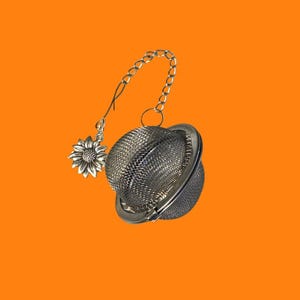 May include: A stainless steel tea infuser with a chain and a sunflower charm. The infuser is spherical with a fine mesh design. The chain and charm are silver-colored, and the background is orange.