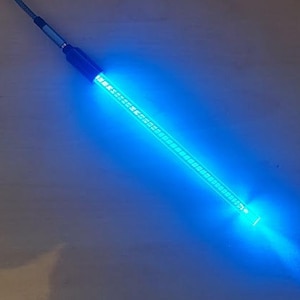 Puede incluir: Una barra de luz LED azul con un mango azul oscuro y un cable. La barra de luz emite un brillo azul brillante. La barra de luz está en ángulo diagonalmente sobre una superficie marrón claro.