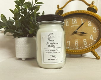 May include: A clear glass jar candle with a black lid and a white label. The label says "Grandma's Cottage" and lists the scents: Lemon, Lavender,  Vanilla, Citronella, Citrus  Soy. The candle is 18 oz and hand-poured in Hawaii.