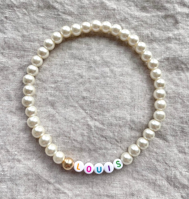 May include: A white pearl necklace with a gold bead and colorful letter beads spelling "LOUIS".