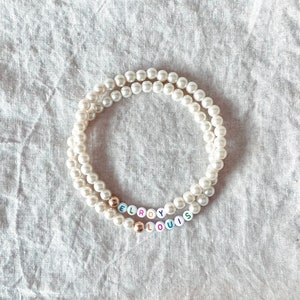 May include: A white pearl necklace with the names "Leroy" and "Louis" spelled out in colorful beads.