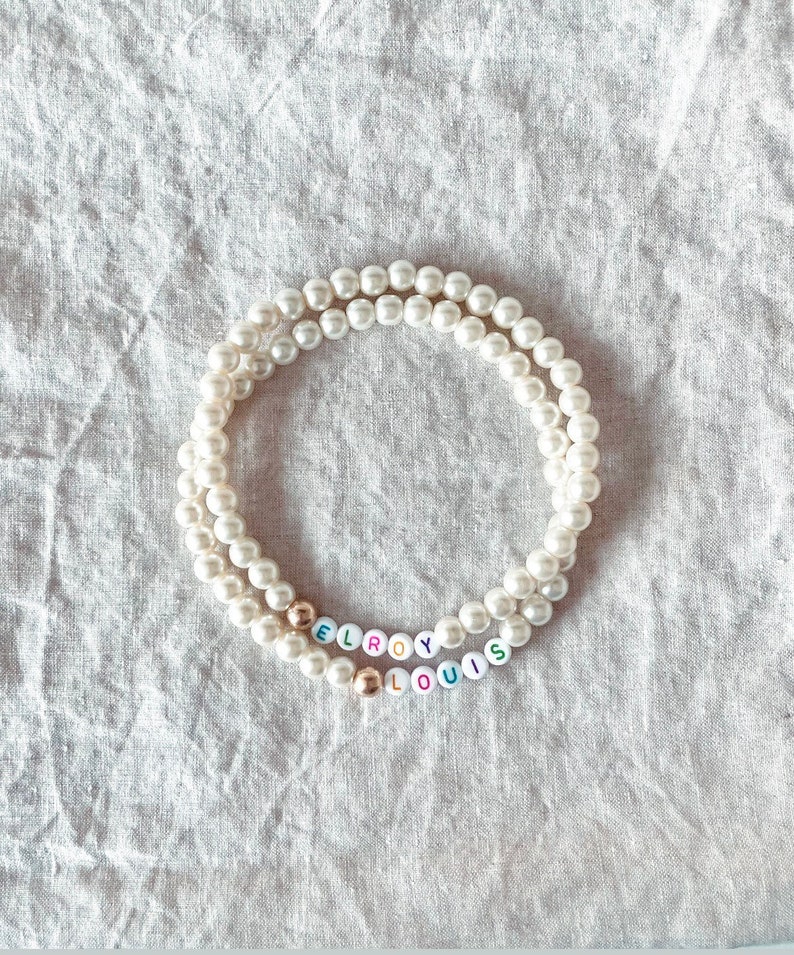 May include: A white pearl necklace with the names "Leroy" and "Louis" spelled out in colorful beads.