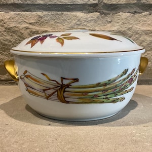 May include: White ceramic serving bowl with a lid, featuring a gold rim and handles. The bowl is decorated with a bundle of asparagus tied with a ribbon. The lid has floral and leaf designs.