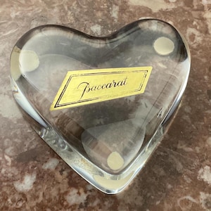 May include: A clear glass heart-shaped paperweight with a gold label that reads "Baccarat".