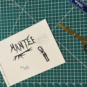 Peut inclure: Un livret blanc avec le titre "HANTEE" écrit en noir, avec une illustration en noir et blanc d'une personne avec une bulle de pensée. Le livret est signé "par Mary Ash".