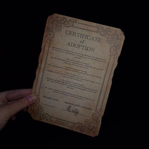 Puede incluir: Un Certificado de Adopci&oacute;n de estilo vintage con bordes ornamentados y texto. El documento tiene un tono sepia, con el t&iacute;tulo "Certificado de Adopci&oacute;n" en la parte superior. Incluye l&iacute;neas para detalles y una firma.