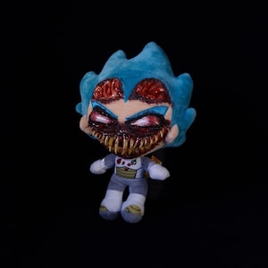 May include: A plush doll with a blue spiky hairstyle and a menacing, open-mouthed face with sharp teeth. The doll wears a gray and white outfit with a chest plate. The eyes are red and the overall design has a horror theme.