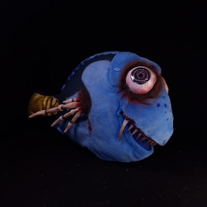 May include: A blue plush toy fish with a large, white eye and sharp teeth. The fish has a bloody, torn open side and a yellow, skeletal fin.