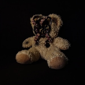 May include: A brown teddy bear with a purple and white octopus tentacle covering its face.